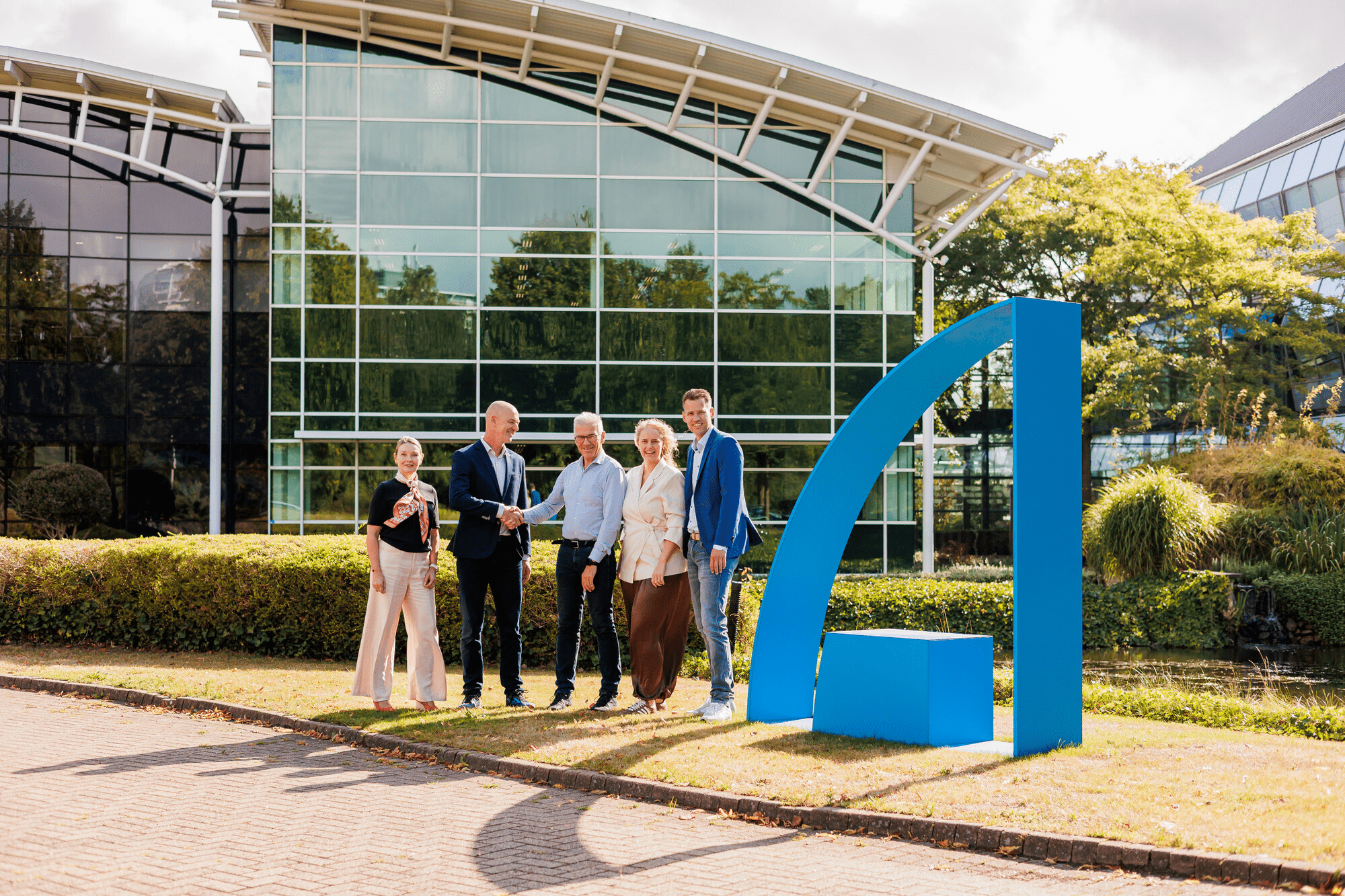 Five representatives from Amgen and Le Champion at Amgen’s office in Breda, standing beside a blue Amgen A-shaped feature.