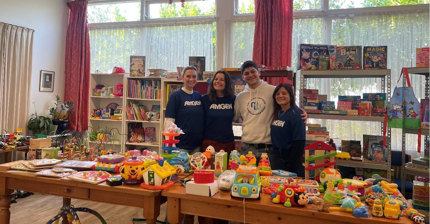 A-group-of-Amgen-colleagues-stands-in-a-space-filled-with-colourful-toys-ready-to-bring-joy-to-children-and-parents-at-Vincentius-banner