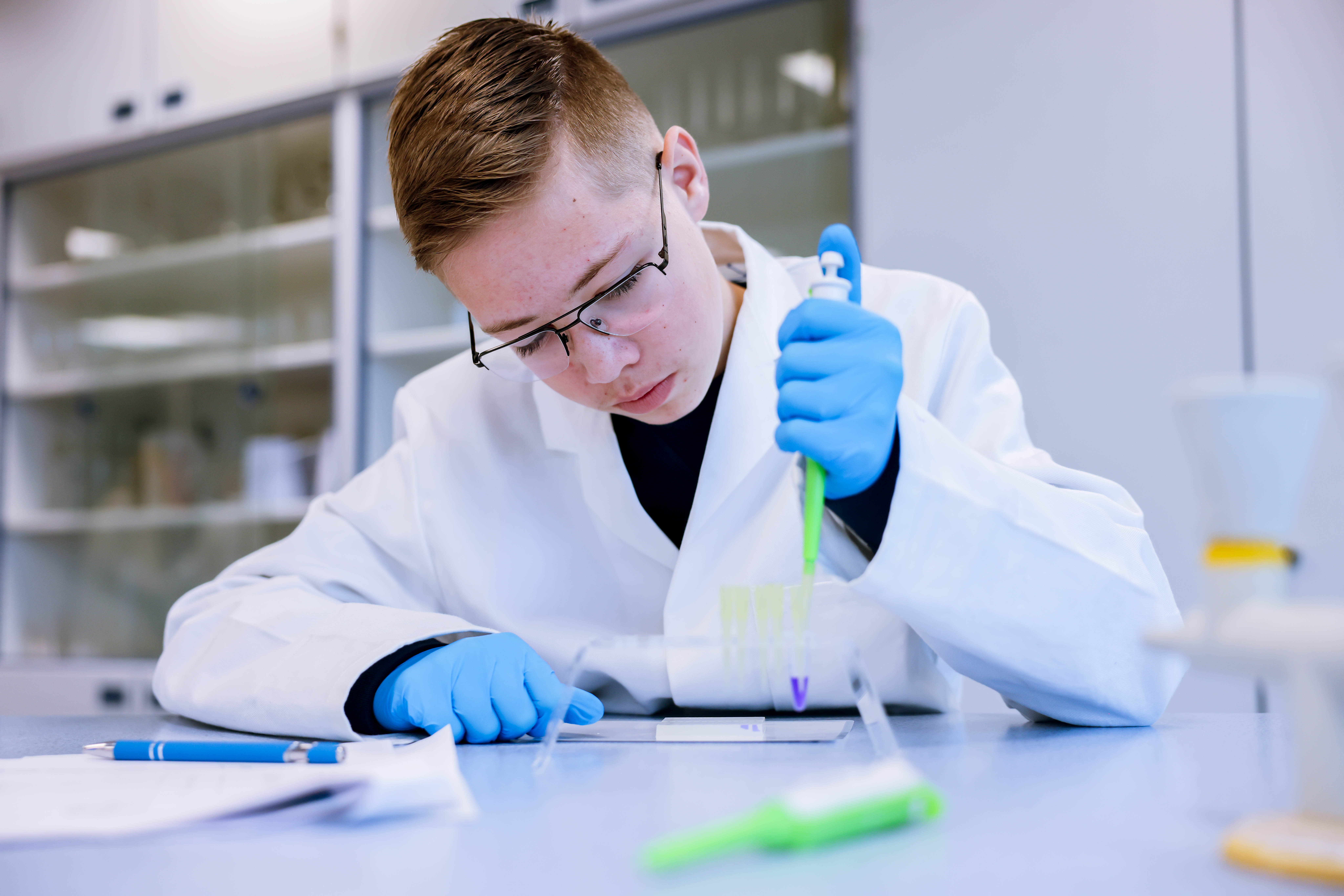 Student carefully pipetting a DNA sample into a gel during a hands-on Amgen Biotech Experience biotechnology experiment in a school laboratory.