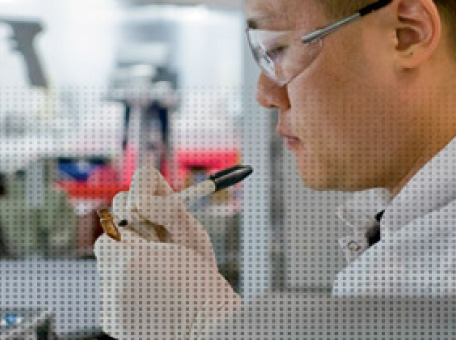 Een Amgen wetenschapper met een veiligheidsbril op heeft een klein flesje in zijn handen waarop hij iets schrijft