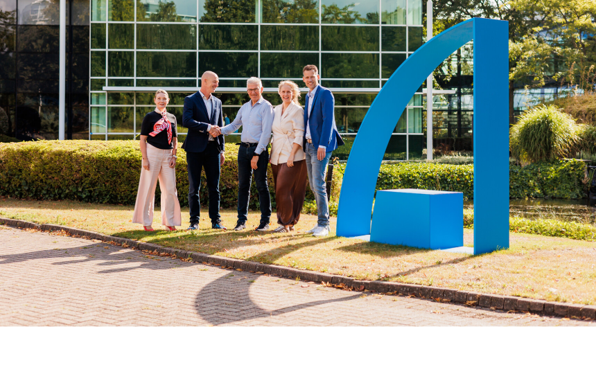 Vijf vertegenwoordigers van Amgen en Le Champion bij het Amgen-kantoor in Breda, naast een blauw Amgen A-element.